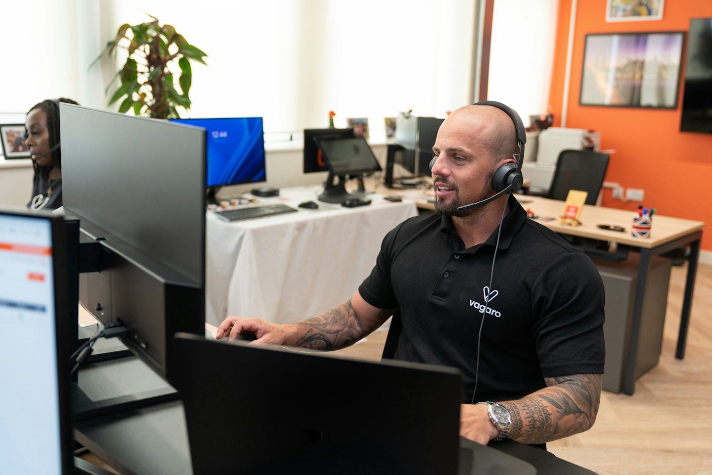 Uomo con barba e tatuaggi con cuffie che lavora a monitor di computer.